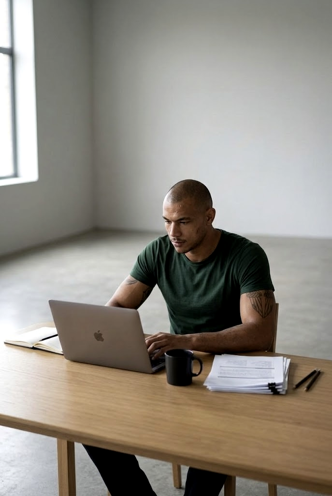 Homem focado ao laptop com parede de concreto ao fundo — concentração e determinação